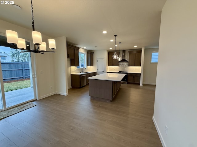 kitchen with light wood-type flooring, a kitchen island, backsplash, wall chimney exhaust hood, and pendant lighting