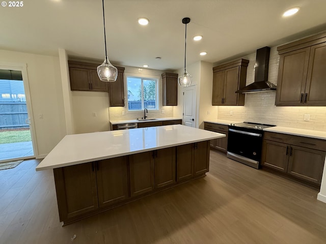 kitchen with sink, stainless steel appliances, wall chimney exhaust hood, and pendant lighting