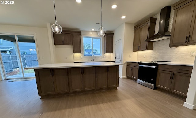 kitchen with decorative light fixtures, light hardwood / wood-style floors, range with electric cooktop, and wall chimney range hood