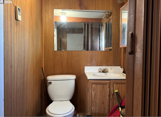 half bath with toilet, vanity, and wooden walls