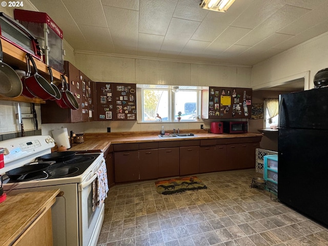 kitchen featuring white stove, black refrigerator, sink, and wood counters