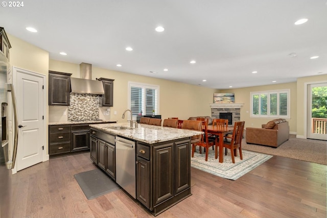 kitchen featuring wall chimney exhaust hood, an island with sink, sink, hardwood / wood-style floors, and appliances with stainless steel finishes