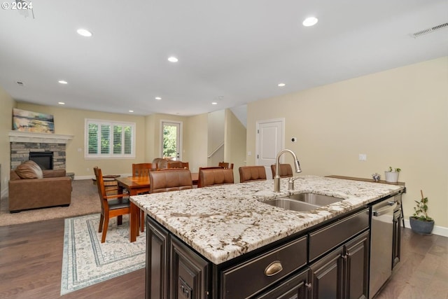 kitchen with sink, a fireplace, dark hardwood / wood-style flooring, stainless steel dishwasher, and a center island with sink