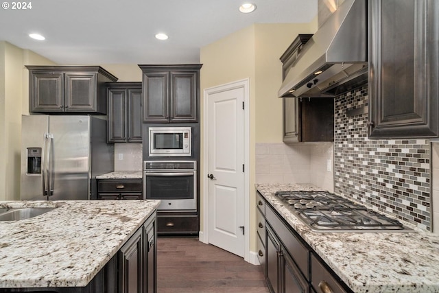 kitchen featuring dark wood-type flooring, wall chimney range hood, stainless steel appliances, and tasteful backsplash