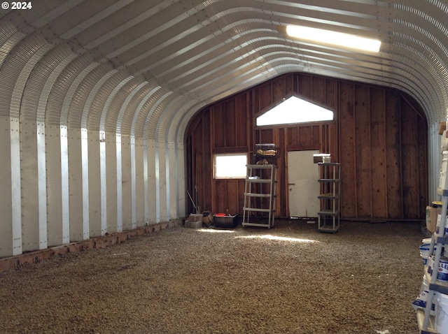 misc room featuring carpet flooring, wooden walls, and vaulted ceiling