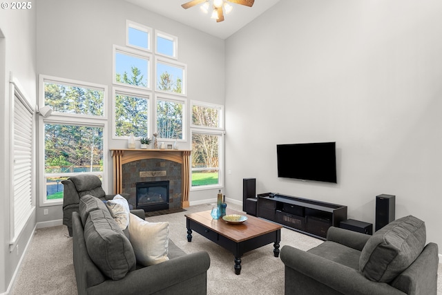 living room featuring a fireplace, a towering ceiling, light colored carpet, and ceiling fan