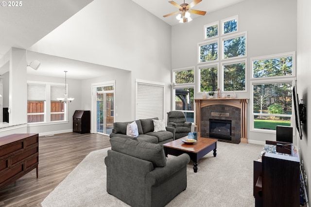 living room featuring ceiling fan with notable chandelier, wood-type flooring, a tile fireplace, and a high ceiling