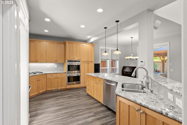 kitchen with light stone countertops, appliances with stainless steel finishes, decorative backsplash, sink, and hanging light fixtures