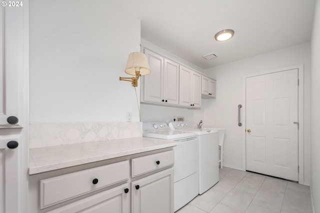 clothes washing area featuring light tile patterned floors, washing machine and clothes dryer, and cabinets