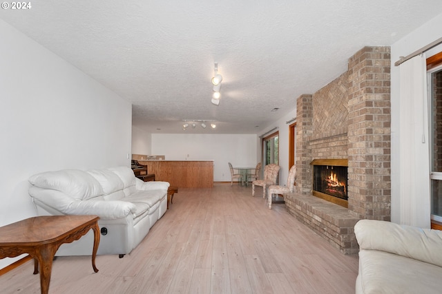 living room with light hardwood / wood-style floors, a textured ceiling, and a brick fireplace