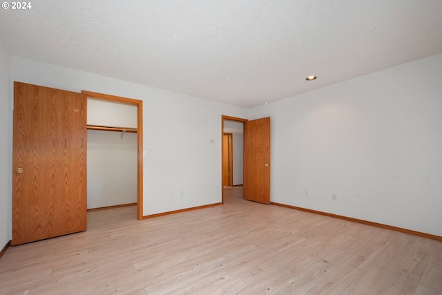 unfurnished bedroom with a closet, a walk in closet, light hardwood / wood-style floors, and a textured ceiling