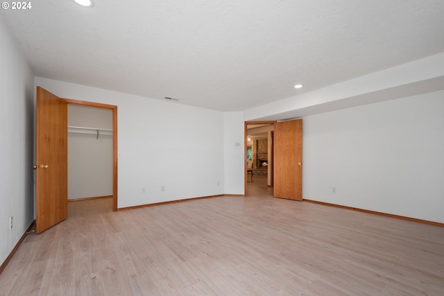 unfurnished bedroom with light wood-type flooring, a closet, a spacious closet, and a textured ceiling