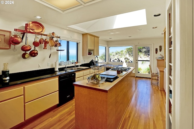 kitchen featuring a skylight, a sink, black dishwasher, light wood-style floors, and a center island