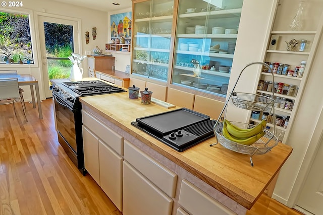 kitchen featuring butcher block countertops, black gas range, light wood-style flooring, and white cabinetry