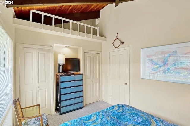 bedroom featuring light colored carpet, two closets, wooden ceiling, and vaulted ceiling with beams