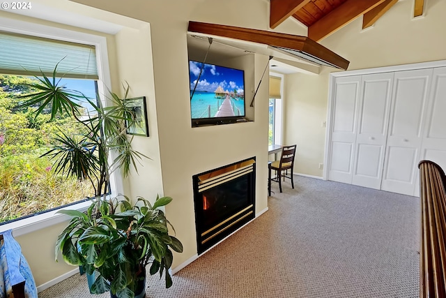 carpeted living area featuring a glass covered fireplace, lofted ceiling with beams, and baseboards