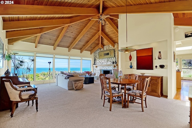 carpeted dining space with ceiling fan, wood ceiling, beam ceiling, a stone fireplace, and high vaulted ceiling