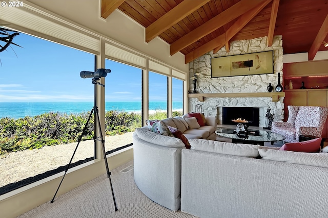 carpeted living area with vaulted ceiling with beams, a view of the beach, a water view, wood ceiling, and a stone fireplace