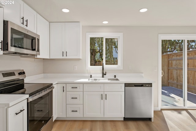 kitchen featuring stainless steel appliances, white cabinetry, light wood-type flooring, and sink