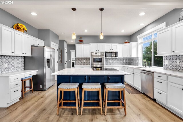 kitchen with a center island, appliances with stainless steel finishes, white cabinets, decorative light fixtures, and light wood-type flooring