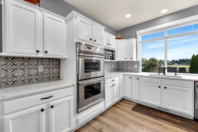 kitchen with sink, tasteful backsplash, white cabinetry, light stone countertops, and stainless steel appliances