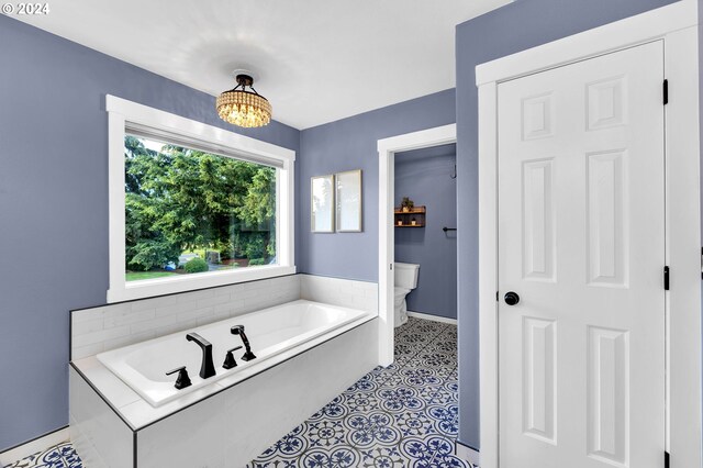 bathroom with tile patterned floors, toilet, a chandelier, and a tub to relax in