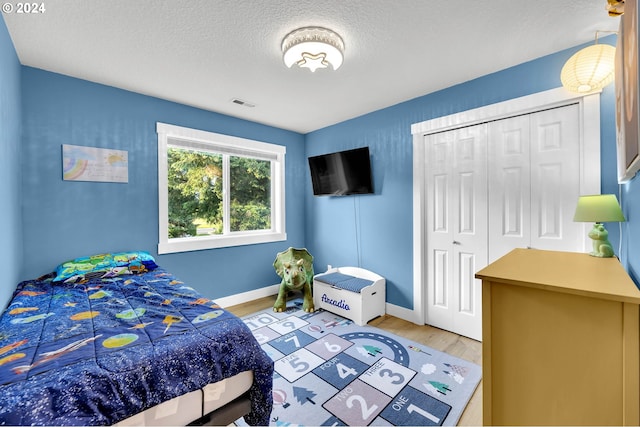 bedroom with a closet, a textured ceiling, and light wood-type flooring