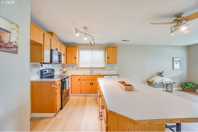 kitchen featuring a sink, black range with electric cooktop, light wood-style floors, light countertops, and stainless steel microwave
