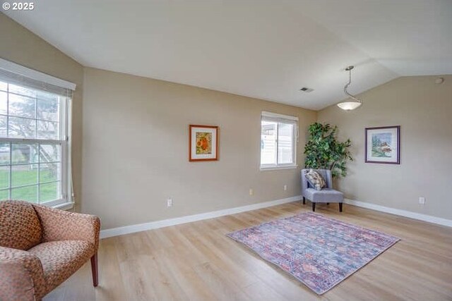 living area with vaulted ceiling, visible vents, light wood finished floors, and baseboards
