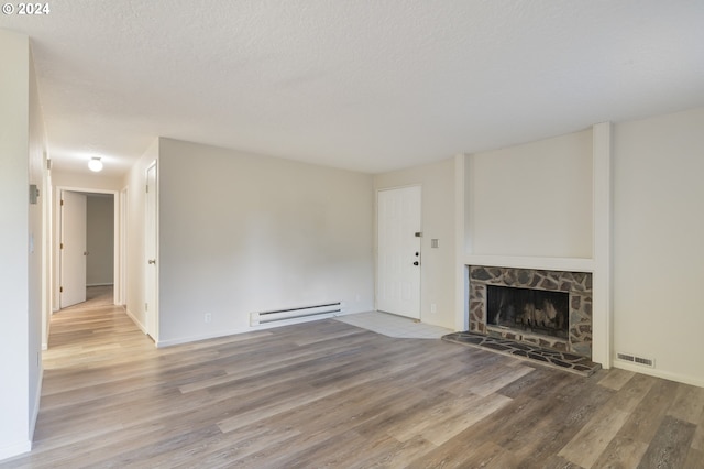 unfurnished living room with hardwood / wood-style flooring, a stone fireplace, a textured ceiling, and baseboard heating