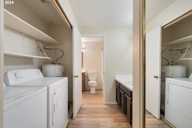 laundry area with water heater, washer and dryer, a textured ceiling, and light wood-type flooring