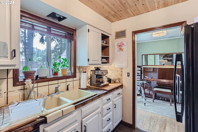 kitchen with tasteful backsplash, plenty of natural light, white cabinetry, black refrigerator, and light hardwood / wood-style flooring