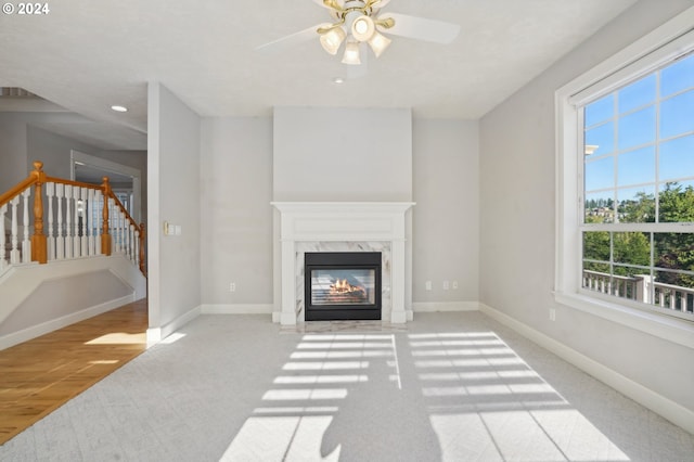 living room with ceiling fan, a high end fireplace, light wood-type flooring, and a healthy amount of sunlight