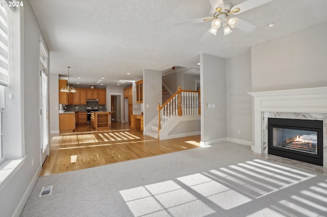 unfurnished living room featuring a fireplace, ceiling fan with notable chandelier, and light wood-type flooring