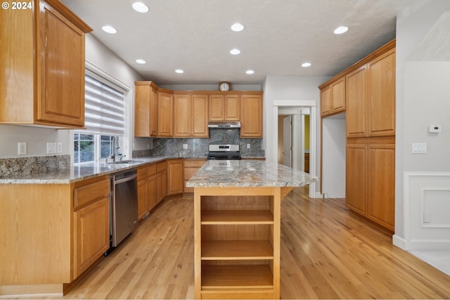 kitchen with light stone countertops, a center island, stainless steel appliances, sink, and light hardwood / wood-style flooring