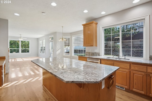 kitchen featuring a kitchen island, light wood-type flooring, stainless steel dishwasher, sink, and hanging light fixtures