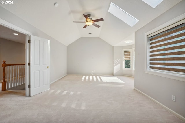 additional living space featuring light carpet, vaulted ceiling with skylight, and ceiling fan