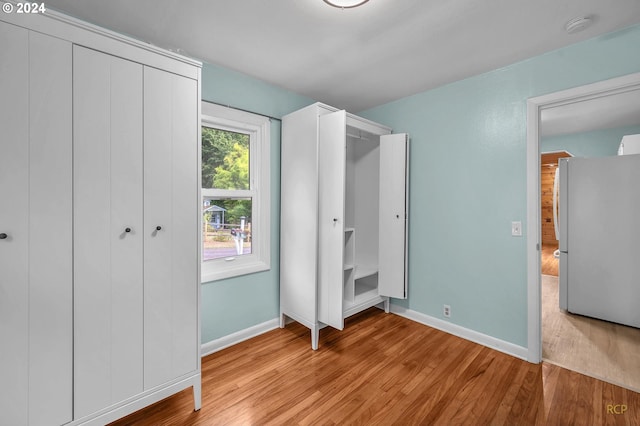 unfurnished bedroom featuring light hardwood / wood-style flooring and white refrigerator