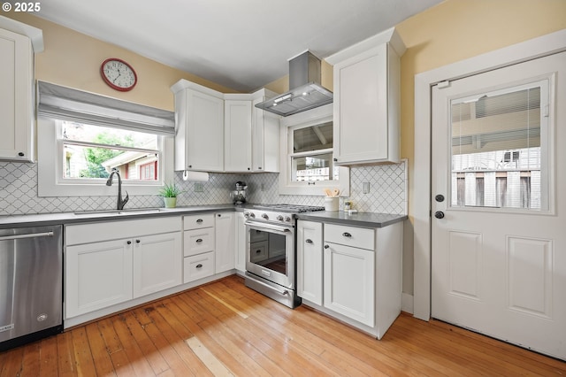 kitchen with a sink, white cabinetry, appliances with stainless steel finishes, wall chimney range hood, and dark countertops