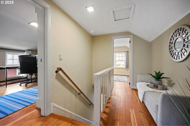 corridor featuring light wood-style floors, a healthy amount of sunlight, vaulted ceiling, and an upstairs landing