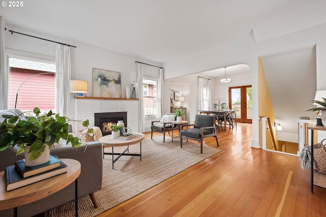 living area featuring french doors, a healthy amount of sunlight, a fireplace, and wood finished floors