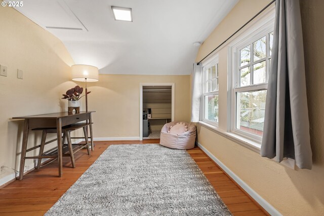 living area with vaulted ceiling, baseboards, and wood finished floors