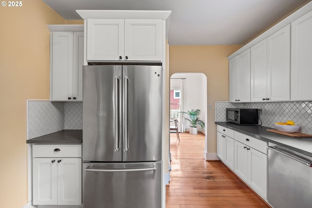 kitchen with stainless steel appliances, dark countertops, light wood-type flooring, and white cabinetry