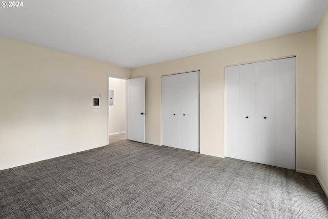 unfurnished bedroom featuring electric panel, multiple closets, and carpet floors