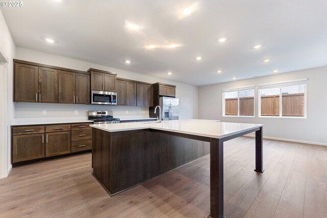 11383 NW 314th Ave, North Plains, OR 97133 - kitchen with stainless steel appliances, light countertops, a kitchen island with sink, dark brown cabinetry, and light wood-style floors