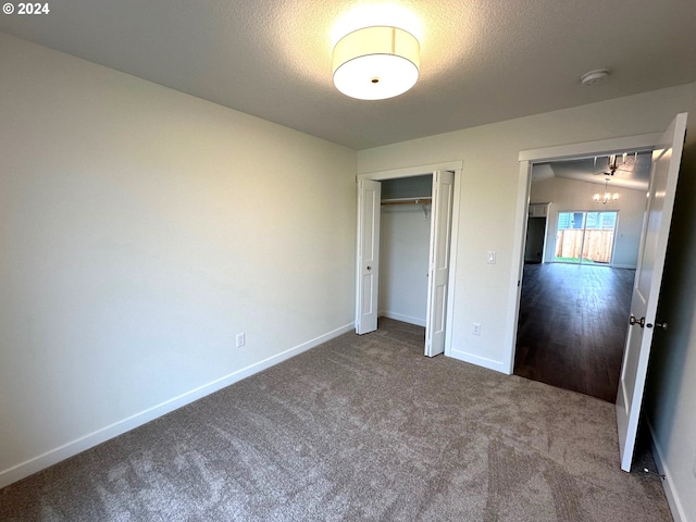 unfurnished bedroom with carpet, a textured ceiling, lofted ceiling, a closet, and a notable chandelier