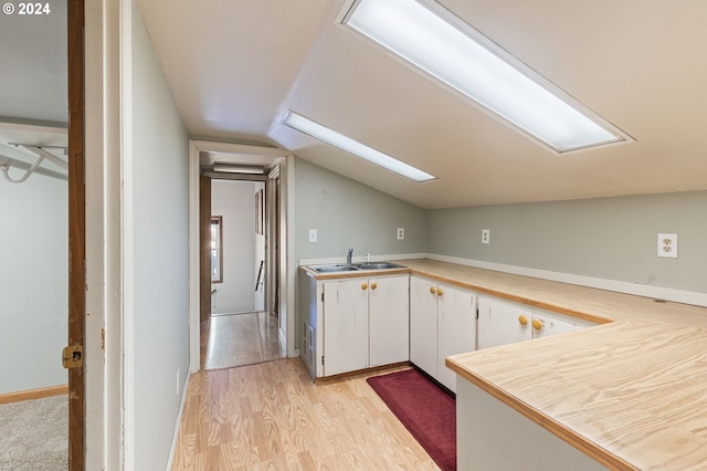 kitchen featuring lofted ceiling, light hardwood / wood-style floors, sink, and white cabinetry