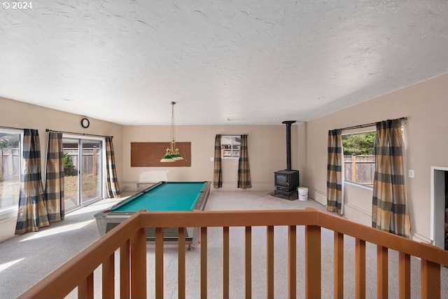 rec room featuring a textured ceiling, a wood stove, carpet flooring, and billiards