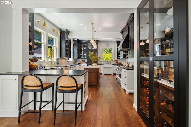 kitchen featuring white cabinets, hanging light fixtures, backsplash, hardwood / wood-style flooring, and a breakfast bar area