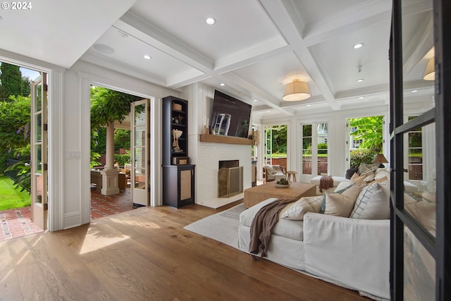 living room with a brick fireplace, a wealth of natural light, light hardwood / wood-style floors, and beamed ceiling